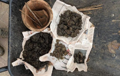 Piles of biodynamic preparations sit on white fabric next to an old terracotta pot with sticks in it, all in a wheelbarrow, creating an earthy, rustic, gardening feel.
