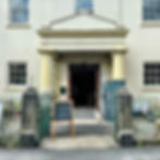 main entrance to the Moor Imagination Centre in Buckfastleigh, Devon, showing large pillars on either side of the covered entrance and metal railings and gate, along with chalkboard signs indicating what is open and what activities and events are happening