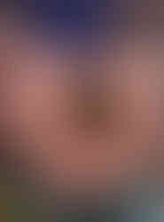 Hands holding a soil with roots showing. Person wears a colorful patterned sweater. Background is blurred, evoking an earthy, natural setting.