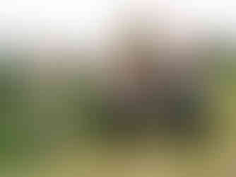 Three people in casual farm attire stand and sit by a red tractor in a lush, rolling hill landscape. They appear cheerful and relaxed.