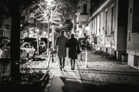 Czarno-białe zdjęcie pary idącej nocą miejską ulicą, widzianej od tyłu.