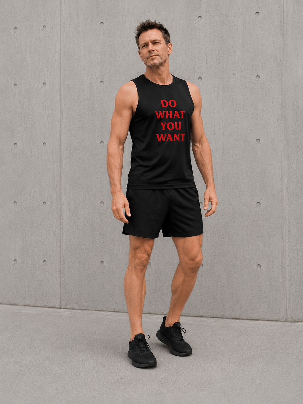 Male model wearing black Do What You Want running vest with black shorts in a minimal urban setting.