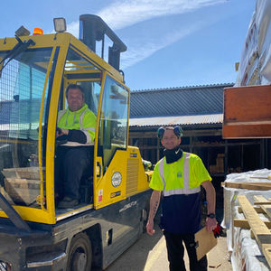 Two men in hi-vis workwear with a yellow forklift in industrial yard.