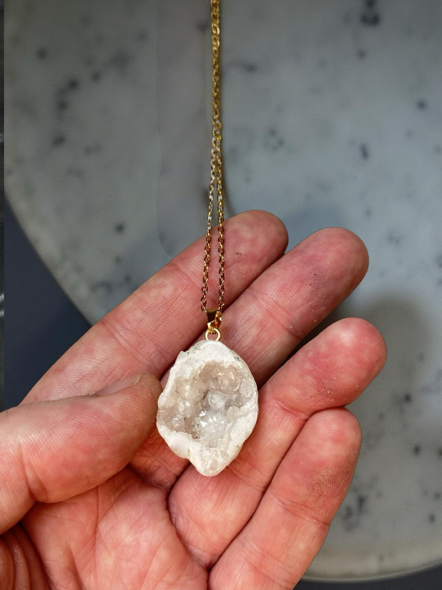 Hand holding a Collier Géode en Cristal de Roche polie percée et montée à la main, collier cristal de roche vertus.