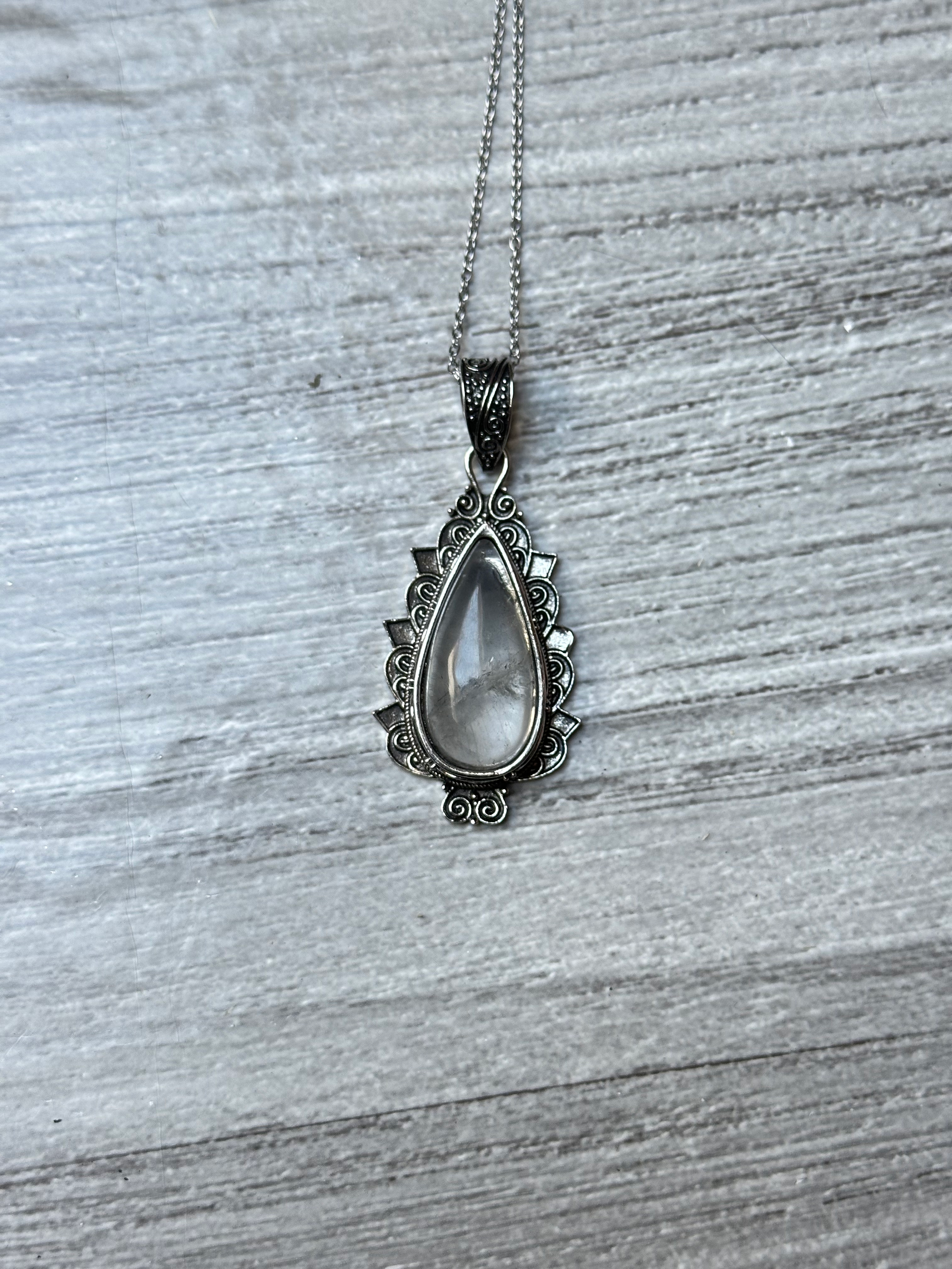 Un collier en cristal de roche suspendu sur une surface en bois. collier “Clarté Bohème” – Cristal de Roche Naturel