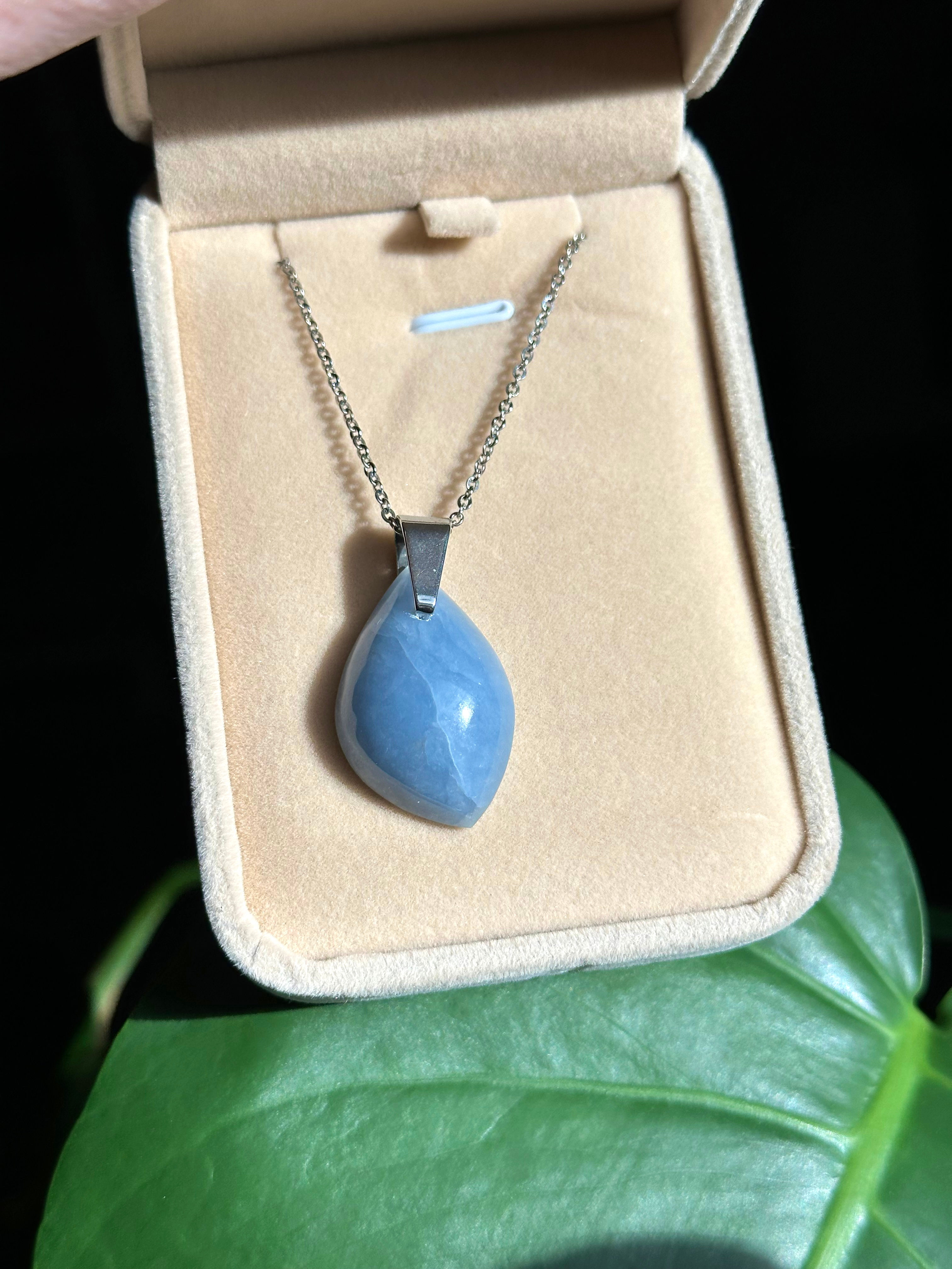 Collier avec pendentif angélite en forme de goutte, sur un présentoir beige. Pierres des anges.