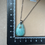 Miniature : Collier avec pendentif turquoise, chaîne argentée, posé sur une surface beige.