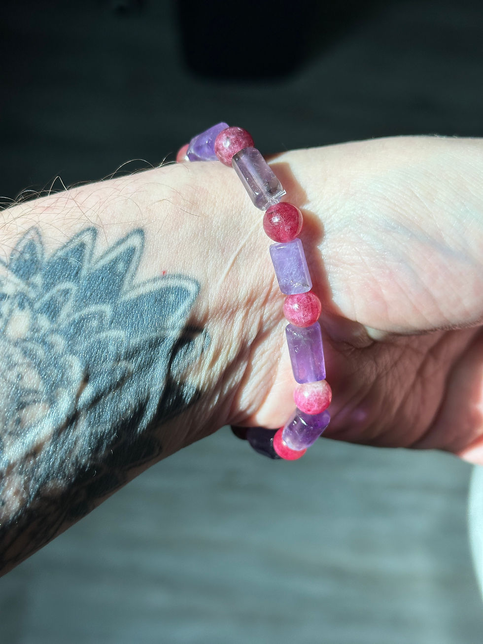 Bracelet de perles violettes et roses sur un bras tatoué