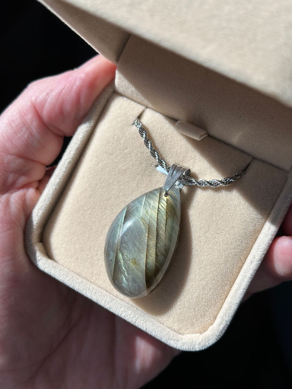 Miniature : Pendentif en pierre irisée dans un écrin, tenu à la main.