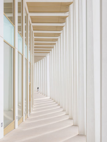 Couloir extérieur blanc moderne vitré et entouré de colonnes.