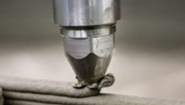 A 3D printer nozzle extruding a line of concrete to form a wall.