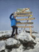 Climber standing at the summit of Mount Kilimanjaro with one hand raised, marking the completion of a high-altitude ascent achieved through safe and responsible trekking.