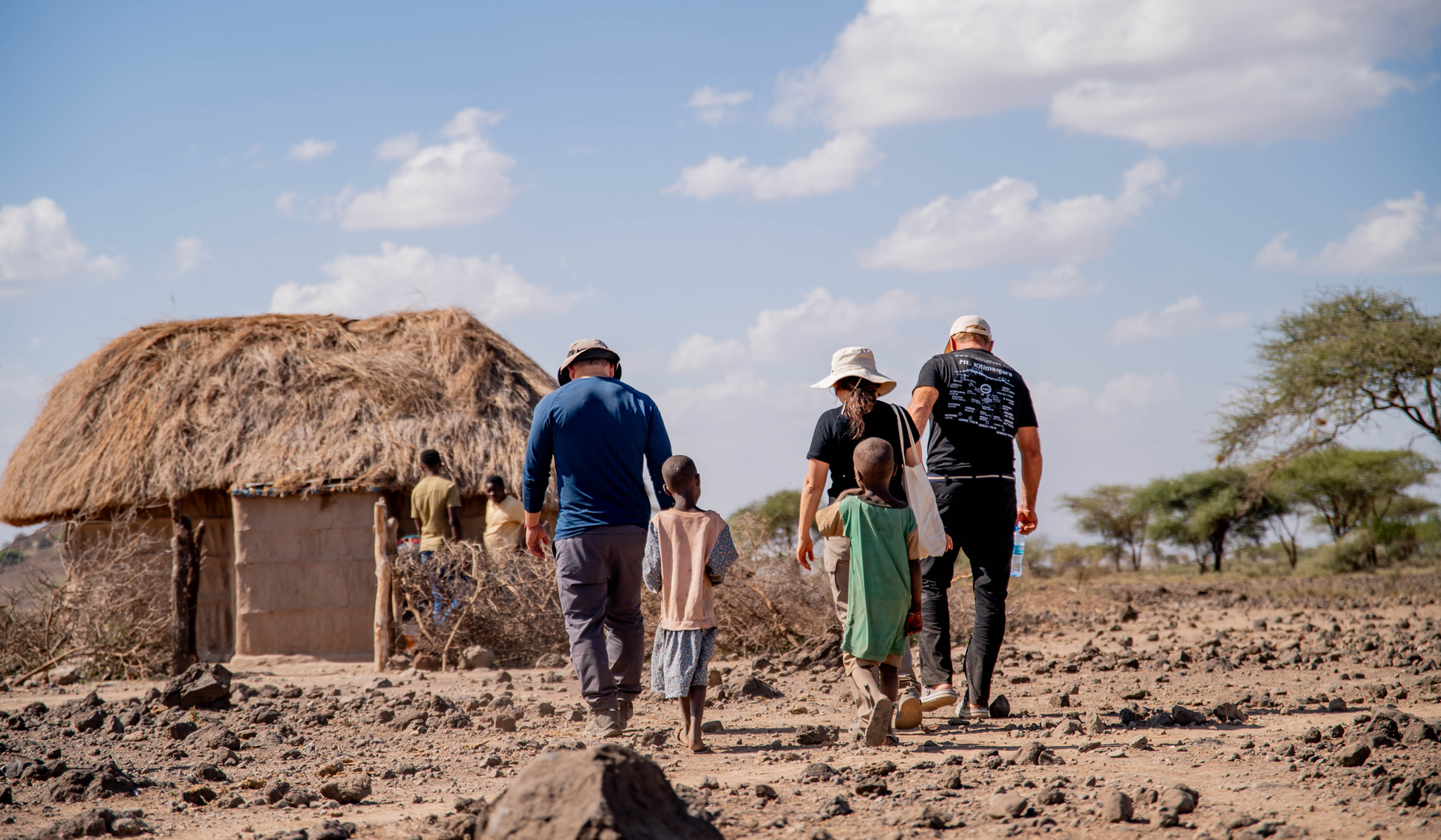 Travelers walking towards a Maasai home in Tanzania during a Kilimanjaro charity climb.