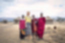 Tourist posing with Maasai people in front of a traditional Maasai village in Tanzania, capturing a cultural moment