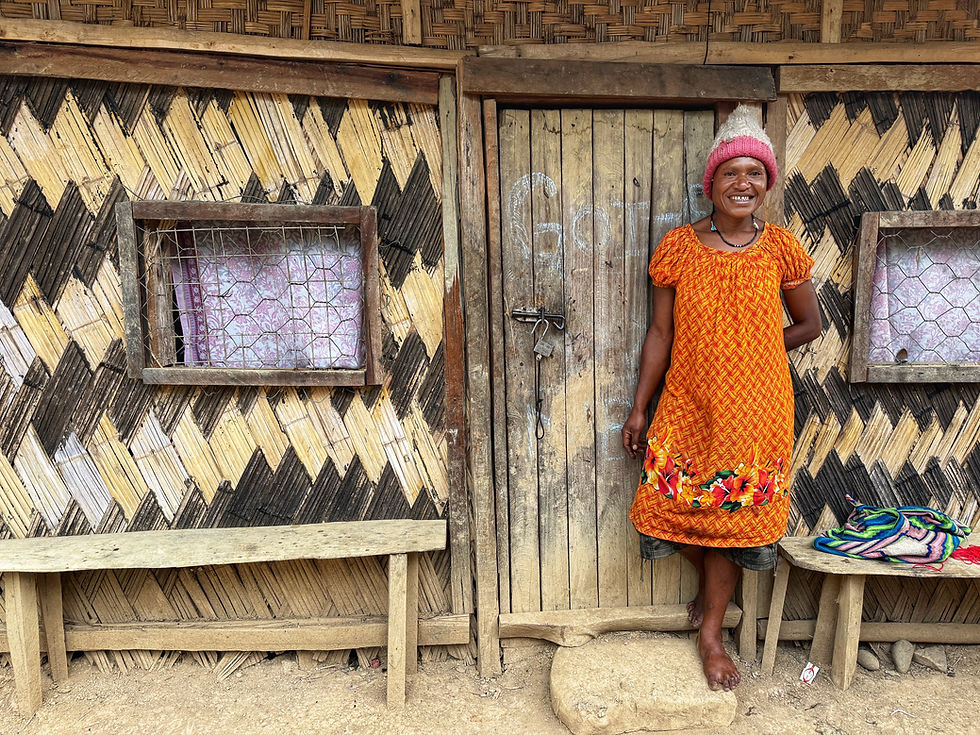 Smiling Papua New Guinean woman standing outside her traditional home in the Highlands of Papua New Guinea.