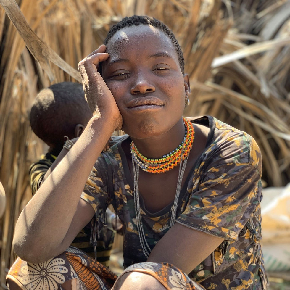 Close up portrait of a Hadzabe woman sitting with her hand on her face, eyes closed and smiling in a hunter gatherer camp near Lake Eyasi, Tanzania.
