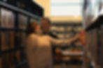 A romantic, playful moment of a couple smiling at each other while browsing library bookshelves