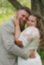 Close-up of a smiling couple embracing outdoors, faces pressed together, wearing wedding attire with a natural background