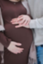 Close-up of a pregnant woman’s belly with two people’s hands gently resting on it, both wearing rings, conveying a calm and i