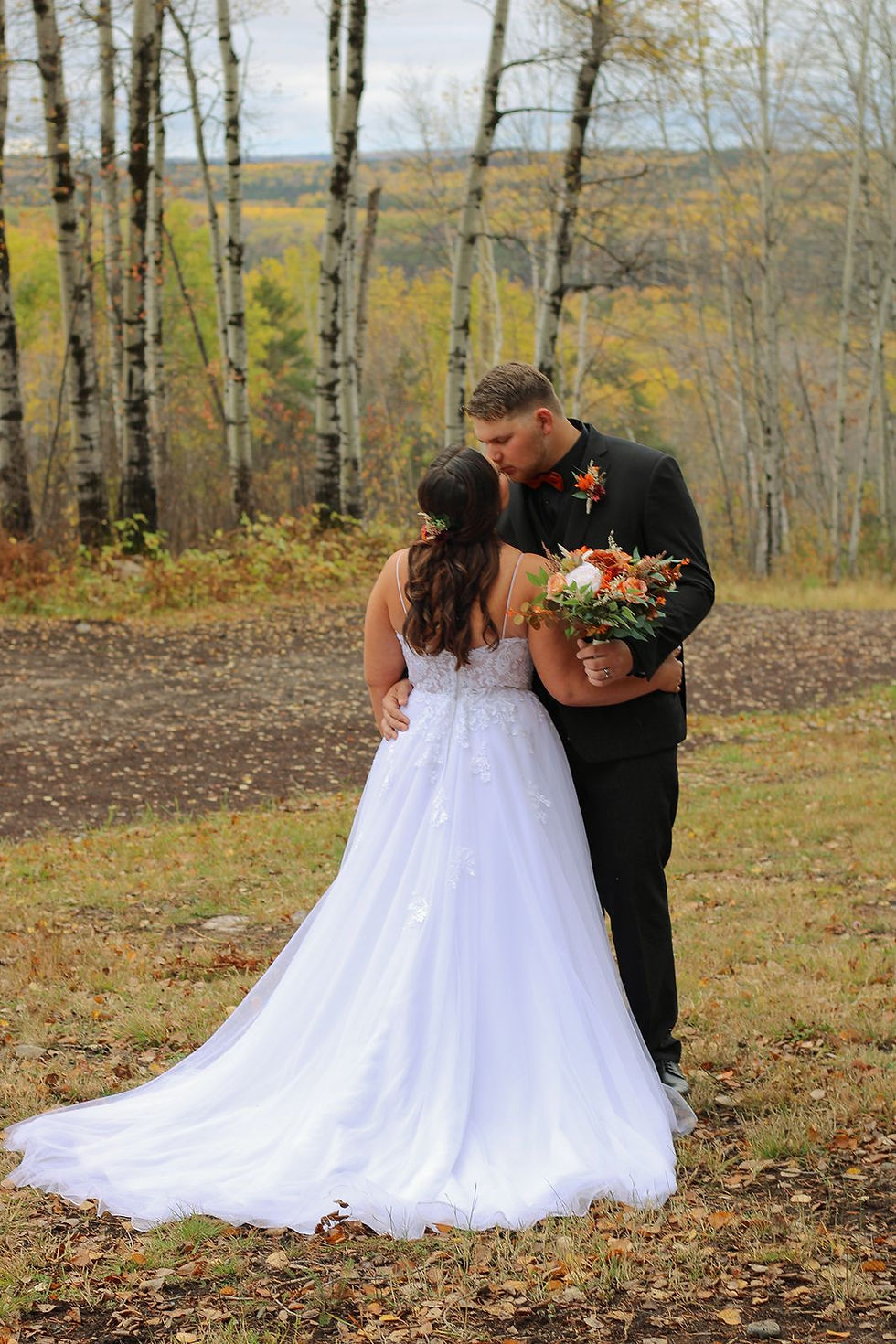 A romantic autumn wedding portrait of a couple kissing against a scenic overlook of vibrant fall foliage