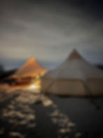 Illuminated bell tent with porch on snowy ground at night, casting soft light. Dark, cloudy sky in the background creates a serene atmosphere.