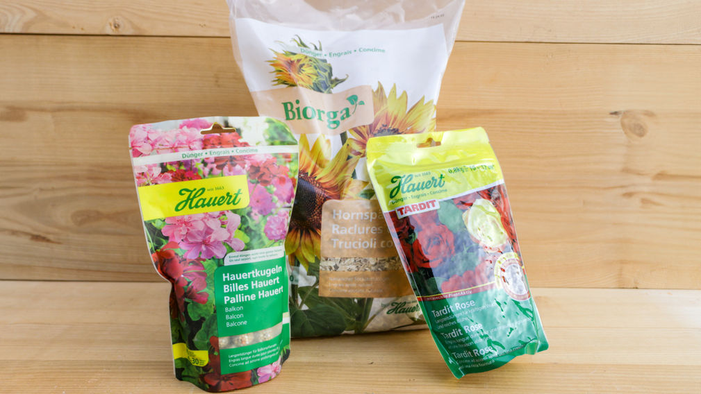 Rosendünger von Hauert, Hauertkugeln und Hornspähne auf einem hellen Holzhintergrund