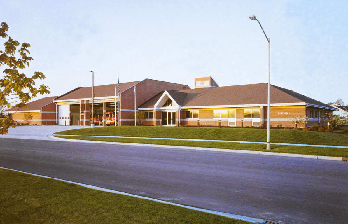 Exterior view of a fire and EMS station with a low-profile building, front entrance, landscaped lawn, and roadway in the foreground.