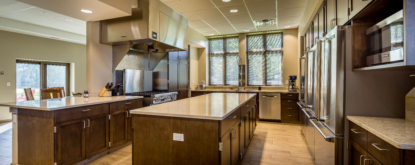 Fire station kitchen and living area with wood cabinetry, central island, stainless steel appliances, and large windows.