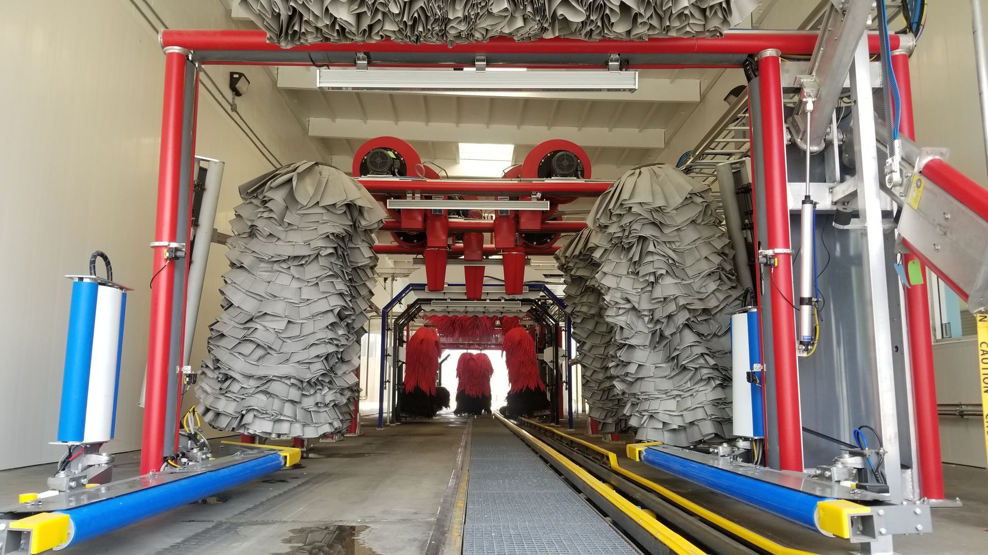 Inside of an automated car wash, red framework with brushes, blue and yellow rails