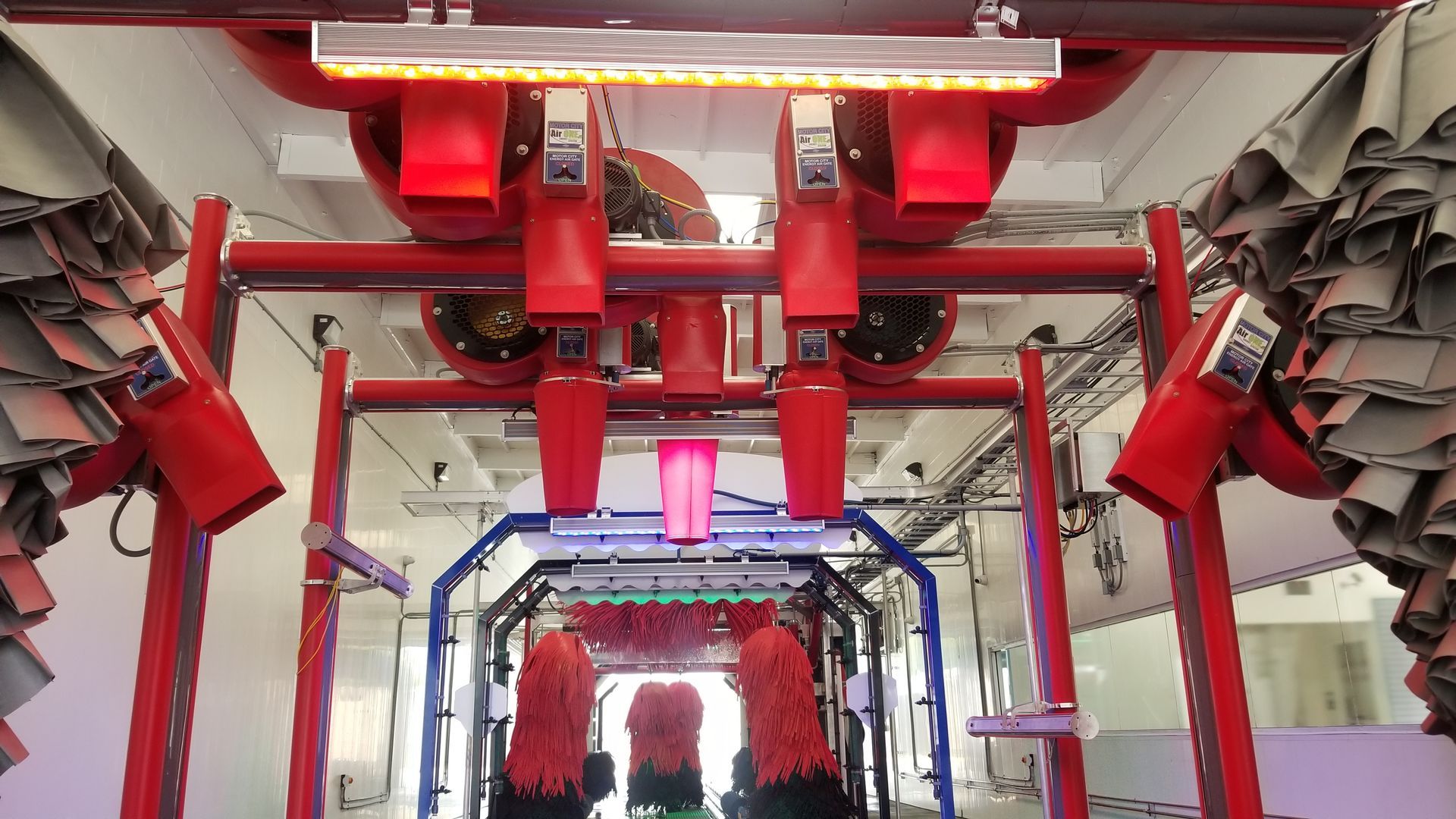 A car wash interior with red and blue machinery, brushes, and lights; viewed from the entrance.