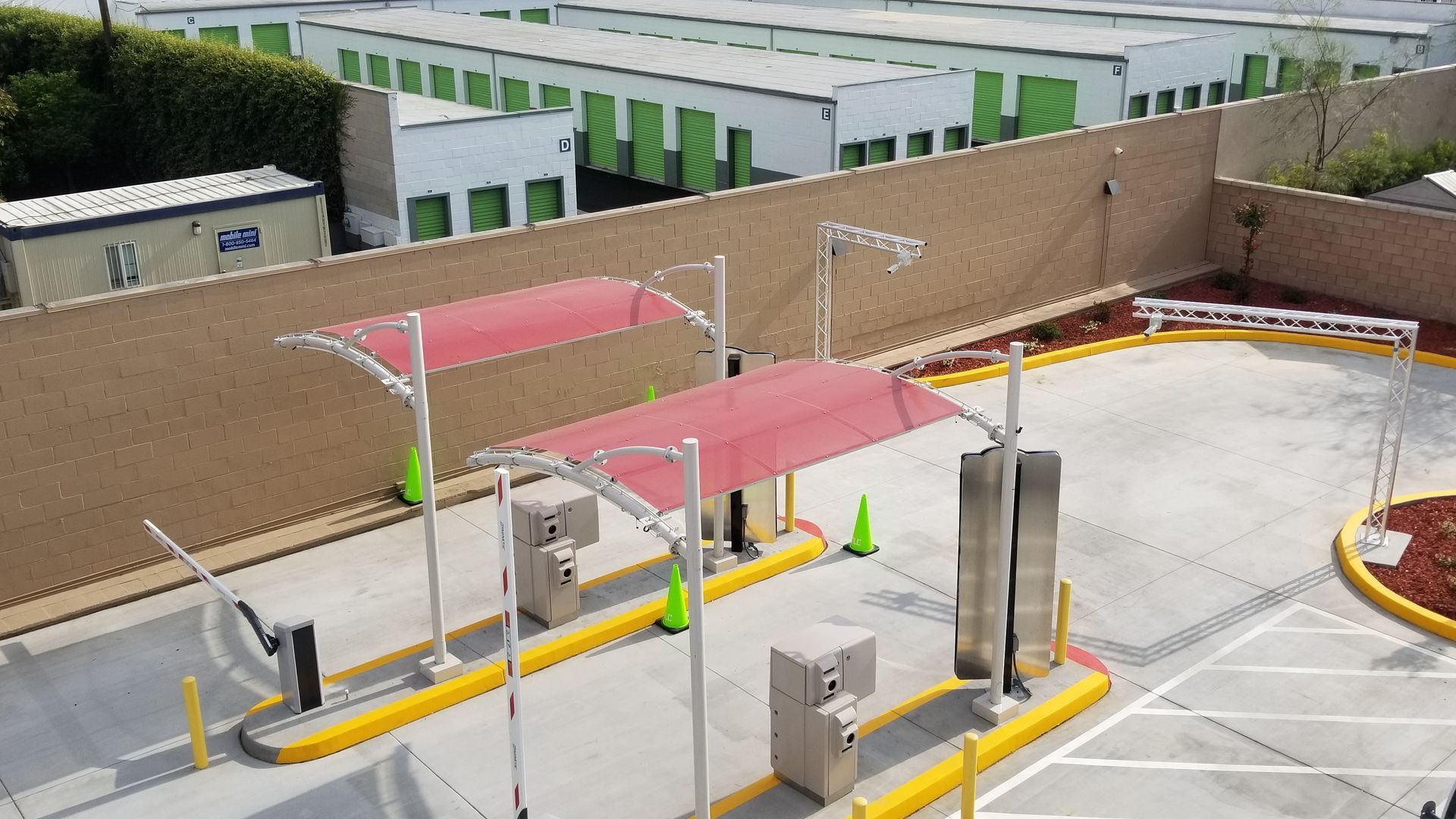 Driveway with two red canopy awnings, entry and exit gates, and storage units in the background.