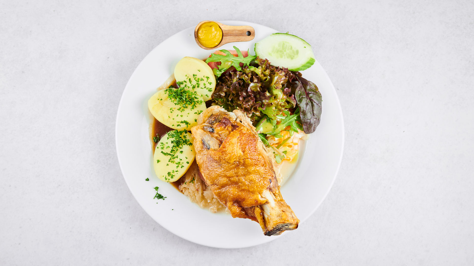 Geschmorte Schweinshaxe mit knuspriger Kruste, serviert in herzhafter Schwarzbiersoße, dazu Sauerkraut, Petersilienkartoffeln und hausgemachter Biersenf.