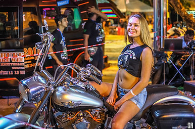 A pretty young woman poses for a photo on a big Harley Davidson motorcycle at Phuket Bike Week