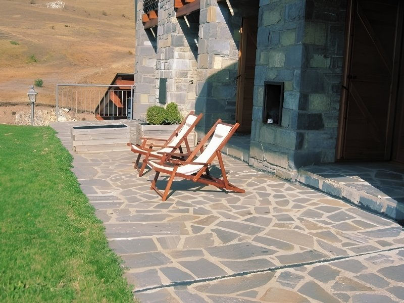 Unregelmässig verlegte Quarzit-Gartenplatten in Natursteinoptik als Terrassenbelag vor einem Gebäude