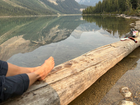 Excerpt from poem Lotus Flower by Barefoot Theology displaying barefoot on a log with a mountains reflected in a still lake in the background
