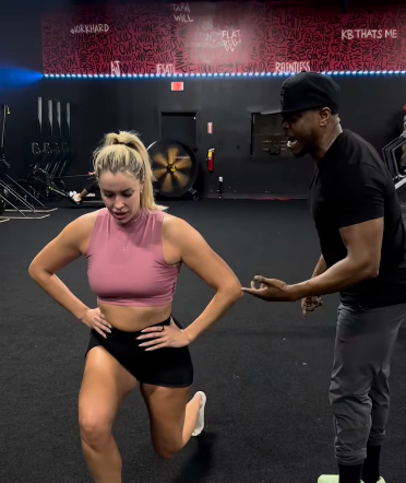 Woman performing lunge assisted by trainer