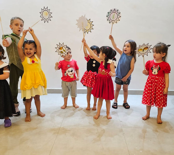 Diversas crianças de 2 e 3 anos seguram acima da cabeça desenhos de sol coloridos presos a um palito.