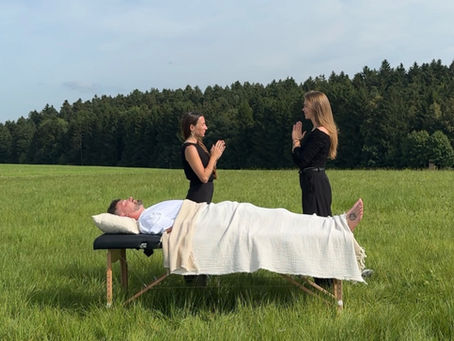 Vanessa und Ela mit einer Behandlungsliege im Grünen auf einer Wiese vor Wald und Himmelpanorama