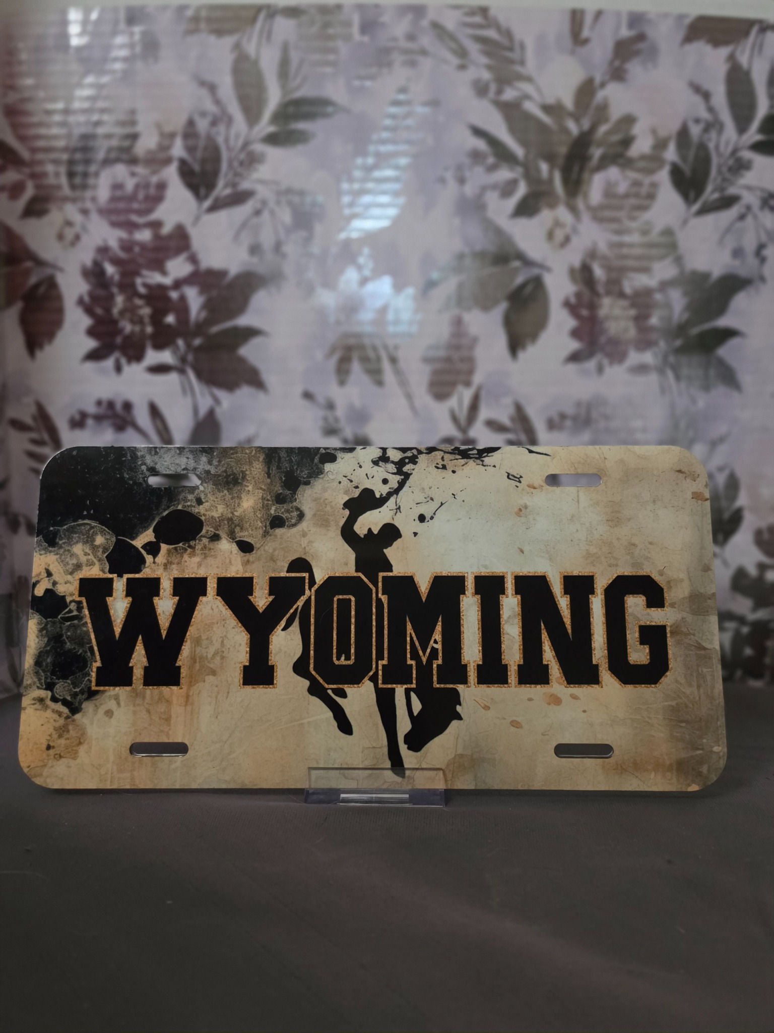 Finished Wyoming decorative license plate with bold black WYOMING lettering and bucking horse and rider on a rustic tan background