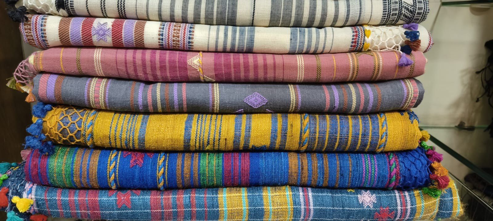 A stack of folded handloom textiles in many colours