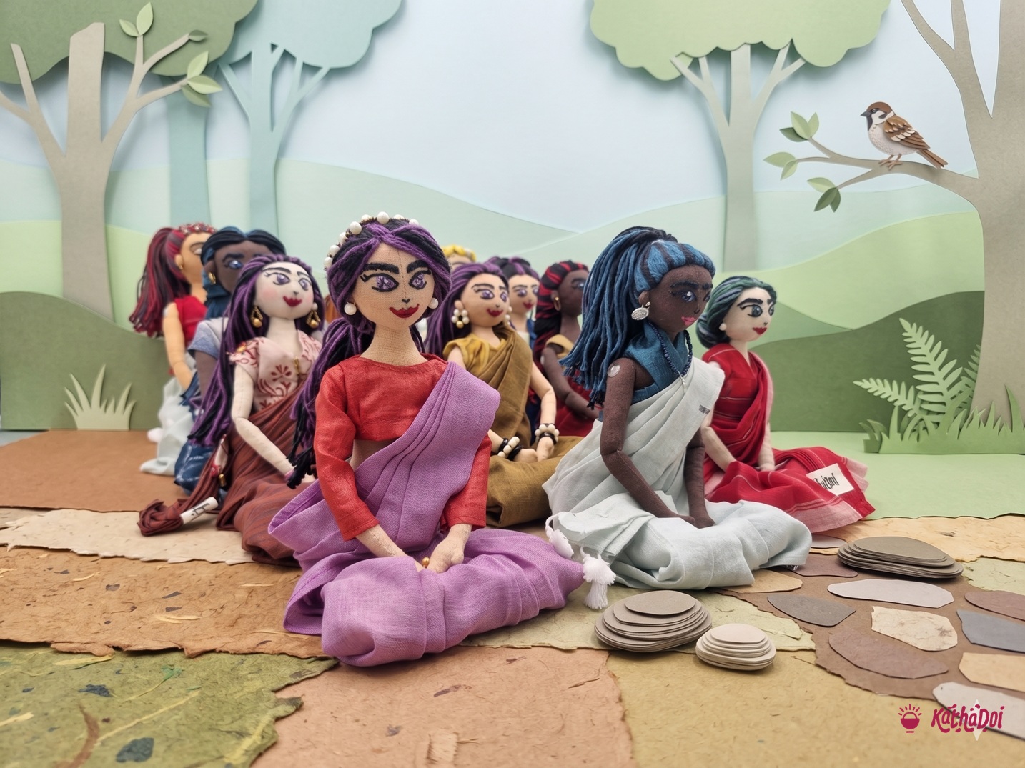 Masakali dolls seated together in handloom saris, against a paper-cut landscape