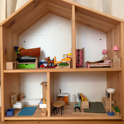 Wooden dollhouse interior with tiny furniture, beds, table, chairs, and lamps; colorful rooms look tidy and cozy.
