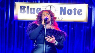 Singer Alex Isley singing on the Blue Note stage in Los Angeles with blue curtains in the background.