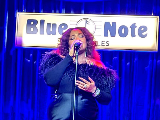Singer Alex Isley singing on the Blue Note stage in Los Angeles with blue curtains in the background.