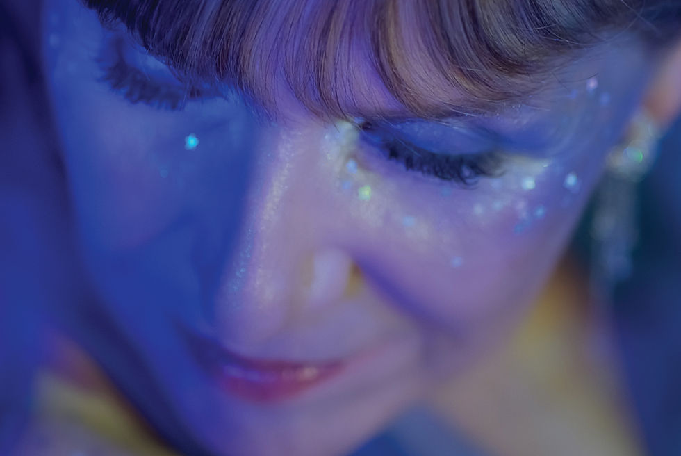 Artist Pauline Frechette close up with sparkles under eyes in a sea of blue.