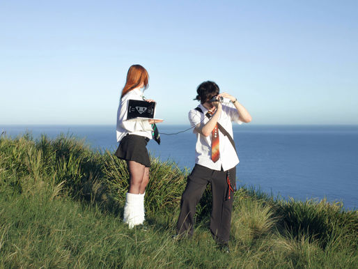 Musicians Ninajirachi and Porter Robinson on a hillside at the water's edge with the sea in the background