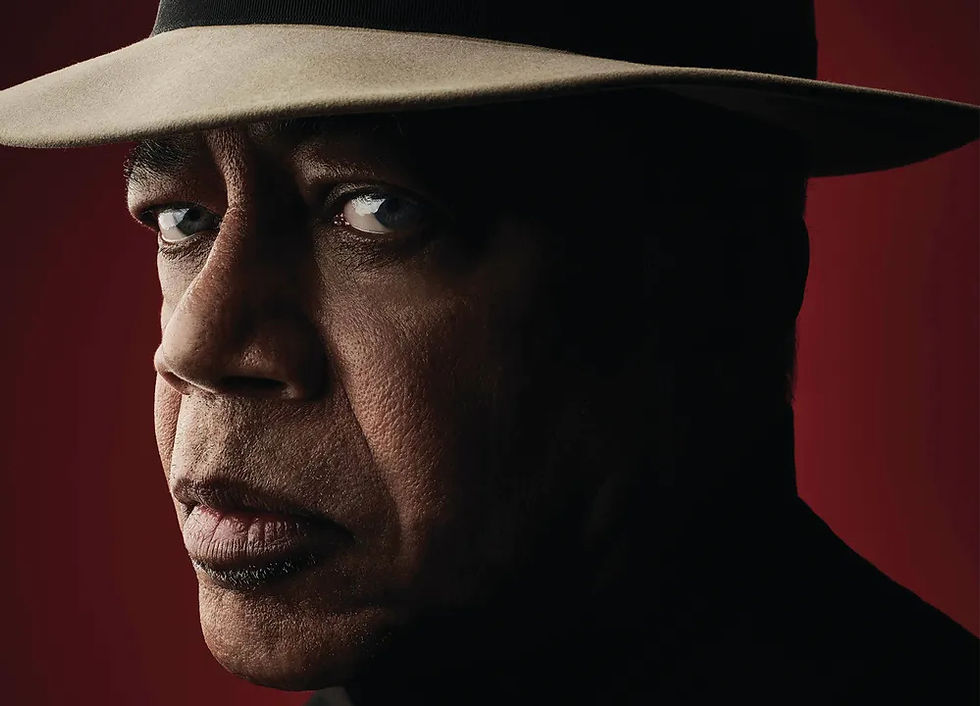 Blues artist Billy Branch on a red background wearing a hat looking into the camera.