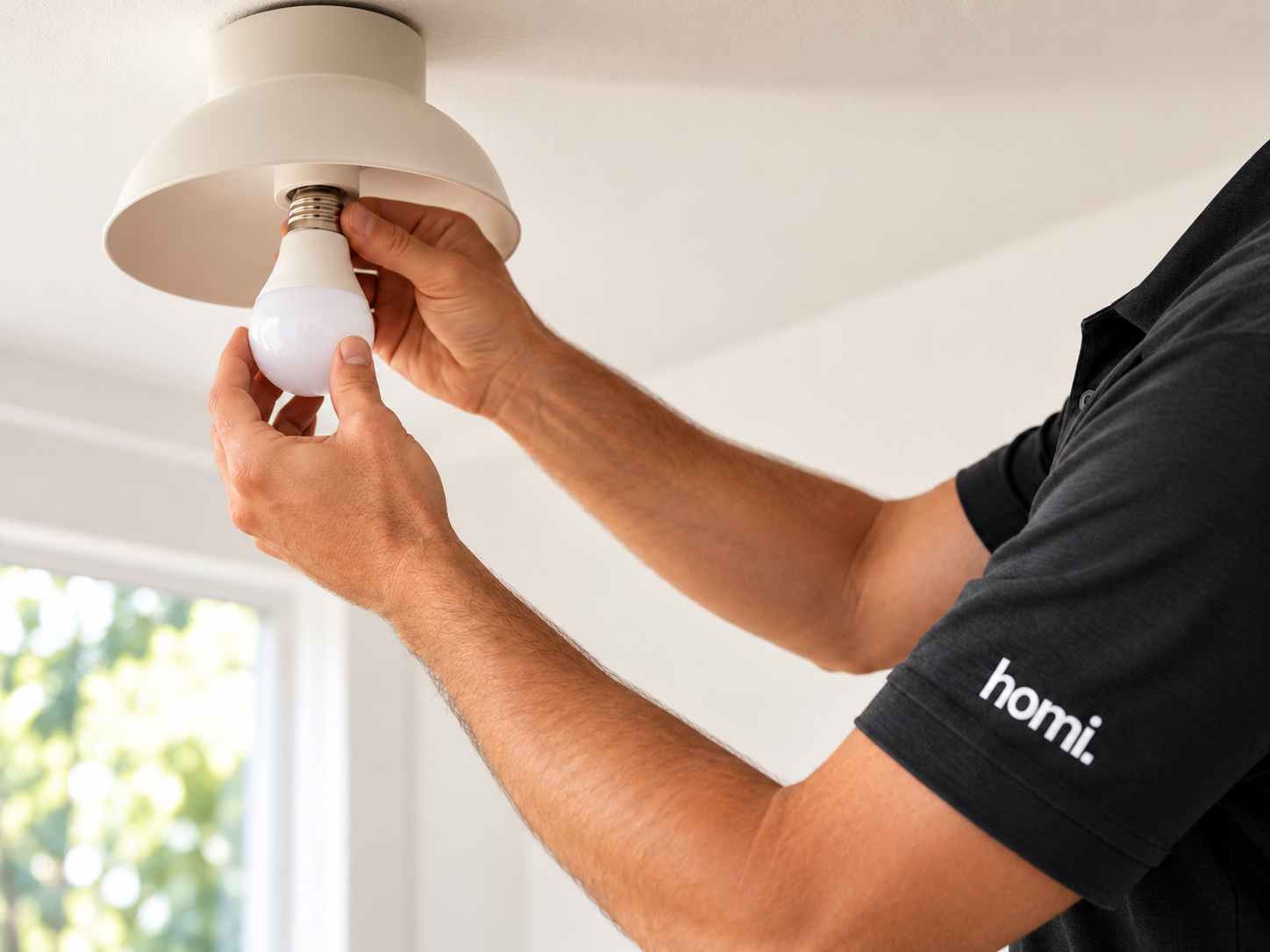 Close-up of a Homi handyman installing a light bulb in a ceiling fixture