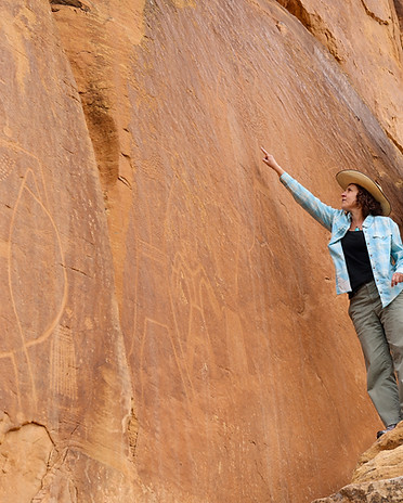Researcher pointing to ancient petroglyphs on a desert rock wall.