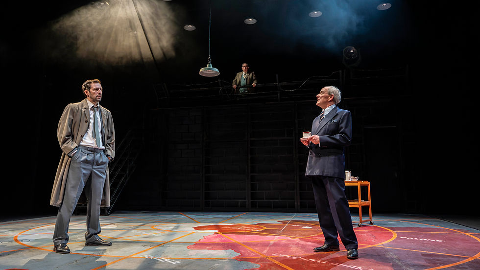Two men in suits face off on a dark stage under spotlights, with a third man on a catwalk and a map floor labeled Poland.